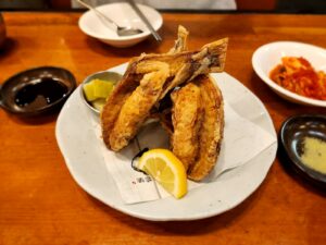 A white plate topped with fried fish next to a bowl of sauce